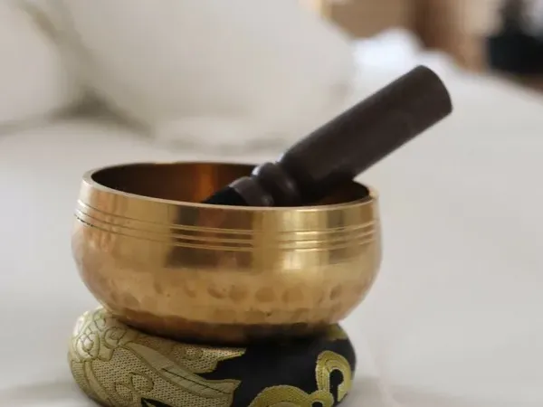 Bol chanteur en laiton et son maillet de bois posés sur la table de soin drapée de blanc