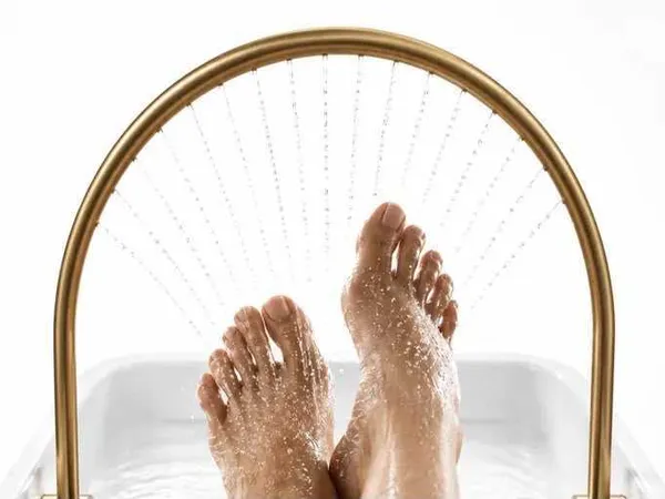 Deux pieds surélevés au-dessus d'un bac, rincés par une arche de jets d'eau dorée