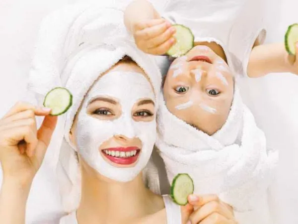 Une mère et son enfant, cheveux enveloppés de serviettes blanches, souriants derrière des rondelles de concombre