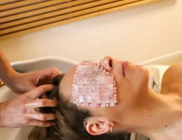 Massage du cuir chevelu au bac, masque de quartz rose sur les yeux, devant le claustra de bois clair